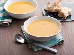 two white bowls filled with soup on top of a wooden table next to silver spoons