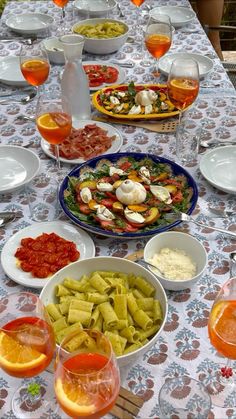 a table topped with lots of plates and bowls filled with different types of food next to wine glasses