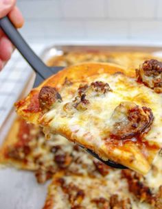 a slice of pizza being held by a spatula with sausage and cheese on it