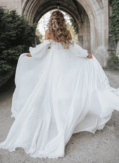 a woman in a white dress is walking through an archway