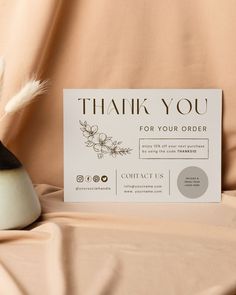 a thank card sitting on top of a table next to a vase with a feather