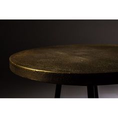 a black table with a gold top on a dark background and white wall behind it