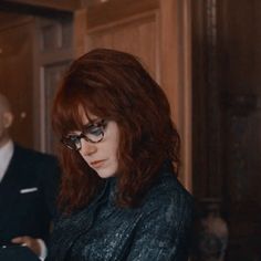 a woman wearing glasses looking at her cell phone while standing next to a man in a suit