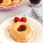 a white plate topped with pancakes covered in jam next to a bowl of strawberries