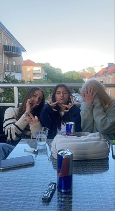 three women sitting at a table with drinks and cell phones in front of their faces