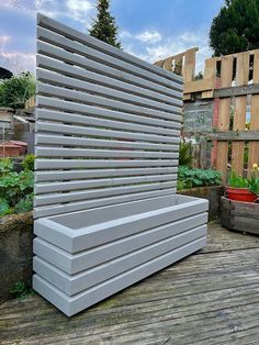 an outdoor bench made out of wooden slats on a deck with potted plants in the background