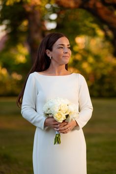 a woman in a white dress holding a bouquet of flowers and looking off into the distance