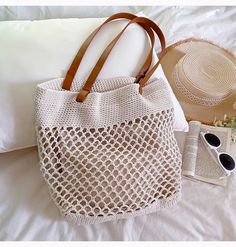 a white bag sitting on top of a bed next to a book and sunglasses in front of a pillow