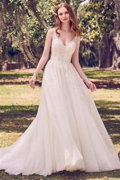 a woman in a white wedding dress standing on the grass with her hands behind her back