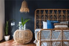 a rattan bed with blue and white pillows in a dark room next to a potted plant