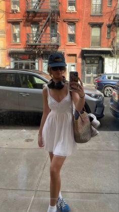 a woman in a white dress and blue shoes taking a selfie with her cell phone