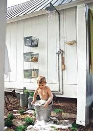 a young boy is washing his hands in a bucket while standing outside an outhouse