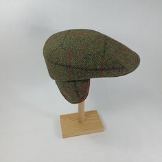 Only size:54cm. Please note that there is no sponge on the visor which is designed to support the fabric. The overall look can be seen in the photos. A timeless, durable and cosy flat cap ideal for autumn and winter, made from authentic Harris Tweed (100% wool). Known for their superior quality, Harris Tweed fabrics stand out from other woollen materials. The cap features a structured peak and a folding, padded earmuff attached to the crown. The folding earmuff not only keeps the ears warm, but also provides additional protection from the cold at the back of the neck. Inside the crown is a soft quilted cotton lining and a cotton sweatband.  WPZ-ANN-HvF-54-v1339 Classic Green Visor Hats, Tweed Winter Cap, Brown Tweed Hats With Herringbone Pattern, Green Wool Cap, Brown Tweed Cap, Adjustable Tweed Flat Cap, Adjustable Plaid Flat Cap, Harris Tweed Fabric, Newsboy Cap