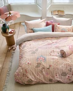 a bed covered in pink and white comforter next to a table with flowers on it