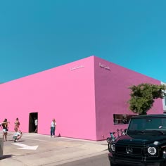 a pink building with people walking by it and cars parked in the parking lot next to it