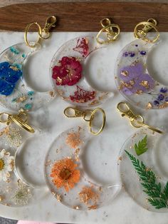 six glass keychains with flowers and leaves on them sitting on a marble surface