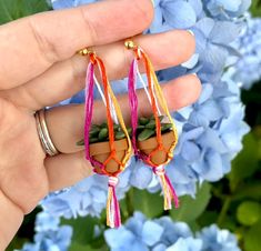 a person is holding two small plants in their hands, one with pink and orange tassels