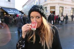 a woman drinking from a red cup while standing in front of a crowd on a city street