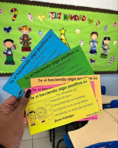 a person holding up three different language cards in front of a classroom wall with children's drawings on it