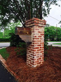 a brick mailbox sitting on top of a pile of mulch next to a tree