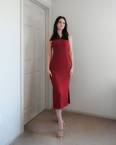 a woman in a red dress standing next to a door and looking at the camera