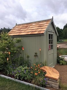 a garden shed with a wooden bench next to it and flowers in the foreground