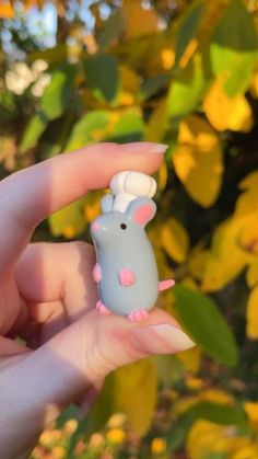 a hand holding a tiny toy mouse in it's left hand with yellow leaves in the background