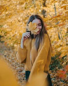 a woman standing in the woods holding a leaf up to her face and looking at it