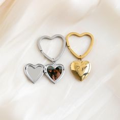 three heart shaped keychains are shown on a white surface, one is gold and the other is silver