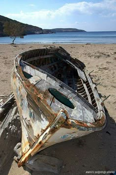 an old wooden boat sitting on top of a sandy beach next to the ocean,