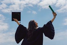 a woman in graduation gown holding up a green diploma cap and tassel over her head