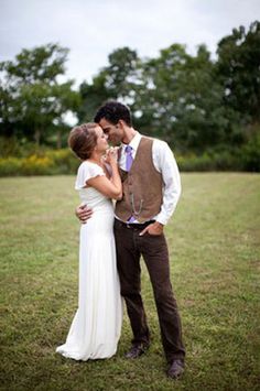 a bride and groom kissing in the middle of a grassy field with trees in the background