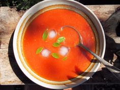 a bowl of tomato soup with ice cubes on the side and a spoon in it