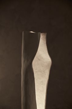 a tall white vase sitting on top of a table next to a light brown wall