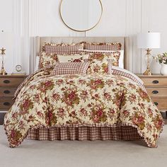 a bed with a floral comforter and pillows on it in a room next to a dresser