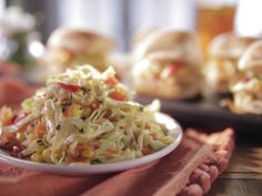 a white plate topped with coleslaw next to rolls