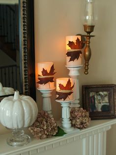 candles are lit on a mantle with autumn leaves