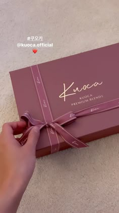 a person is opening a pink box with a ribbon on the top and writing on it