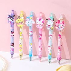 five hello kitty pens are lined up against a pink wall with other items on it