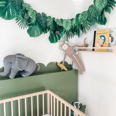 a baby crib with stuffed animals and green leaves hanging on the wall above it