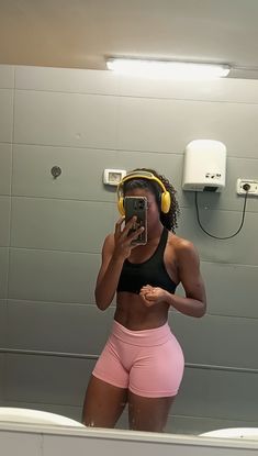 a woman taking a selfie in front of a mirror wearing headphones and pink shorts