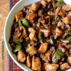 a white bowl filled with chicken and peppers on top of a wooden table next to a purple place mat