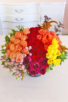 a vase filled with lots of colorful flowers on top of a white table next to a dresser