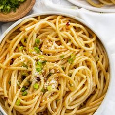 a white bowl filled with pasta and topped with parmesan cheese, scallions and chopped green onions