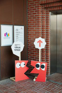 two street signs with faces on them in front of a brick wall and door way