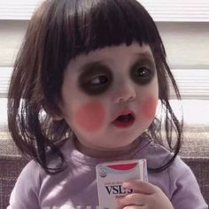 a doll with black makeup holding a box of vise eyeliners in front of her face