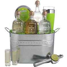 a metal bucket filled with liquor bottles and garnished with limes next to two shot glasses