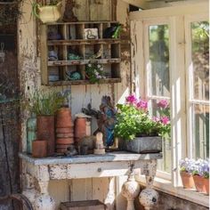 an old table with potted plants on it in front of a window filled with pots and panes