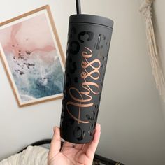 a person holding up a black and rose gold travel mug with the word love on it