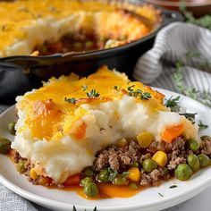 a white plate topped with mashed potatoes covered in meat and veggies next to a casserole dish